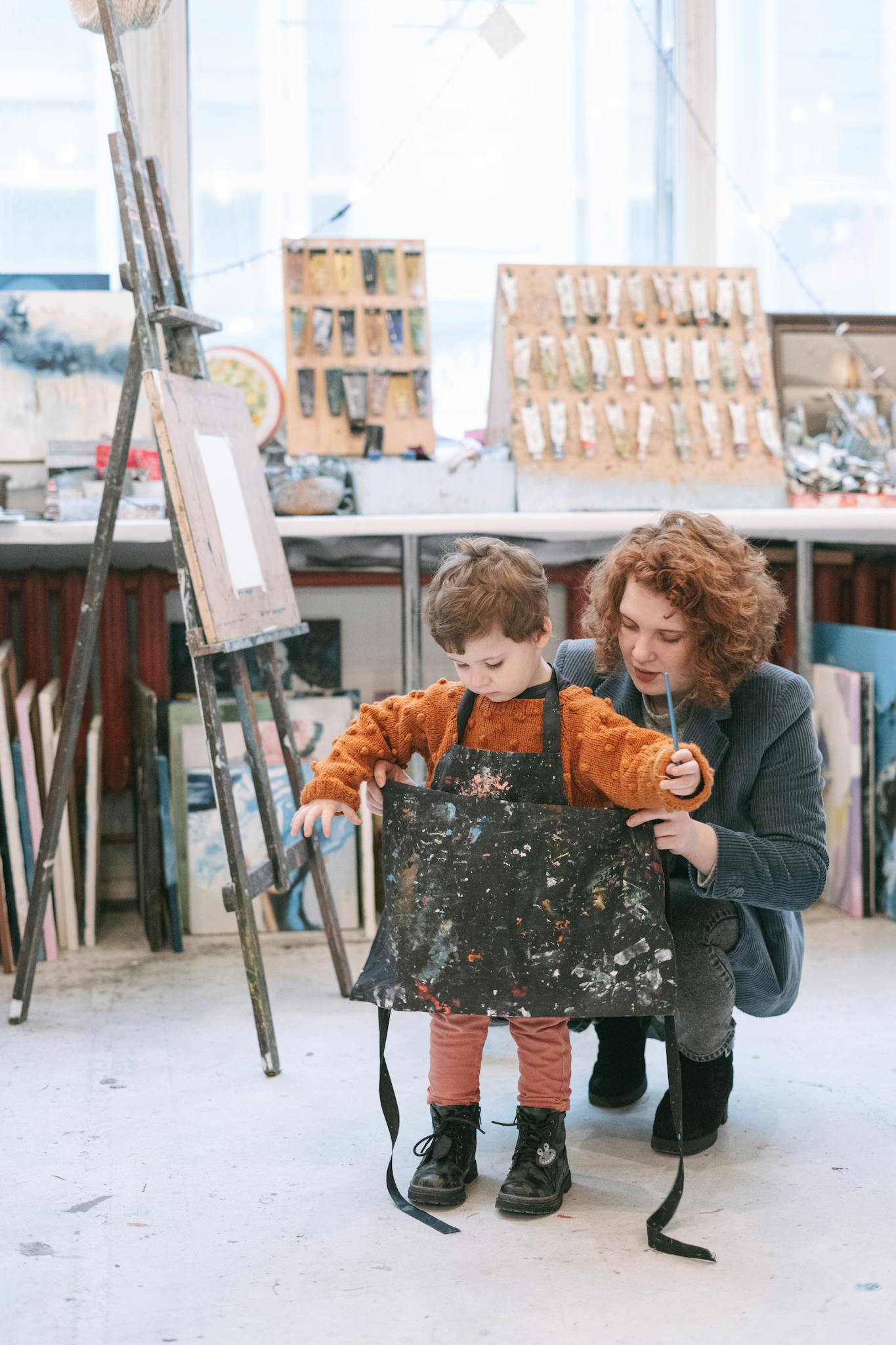 A mother assists her child with an apron in a creative art studio setting.