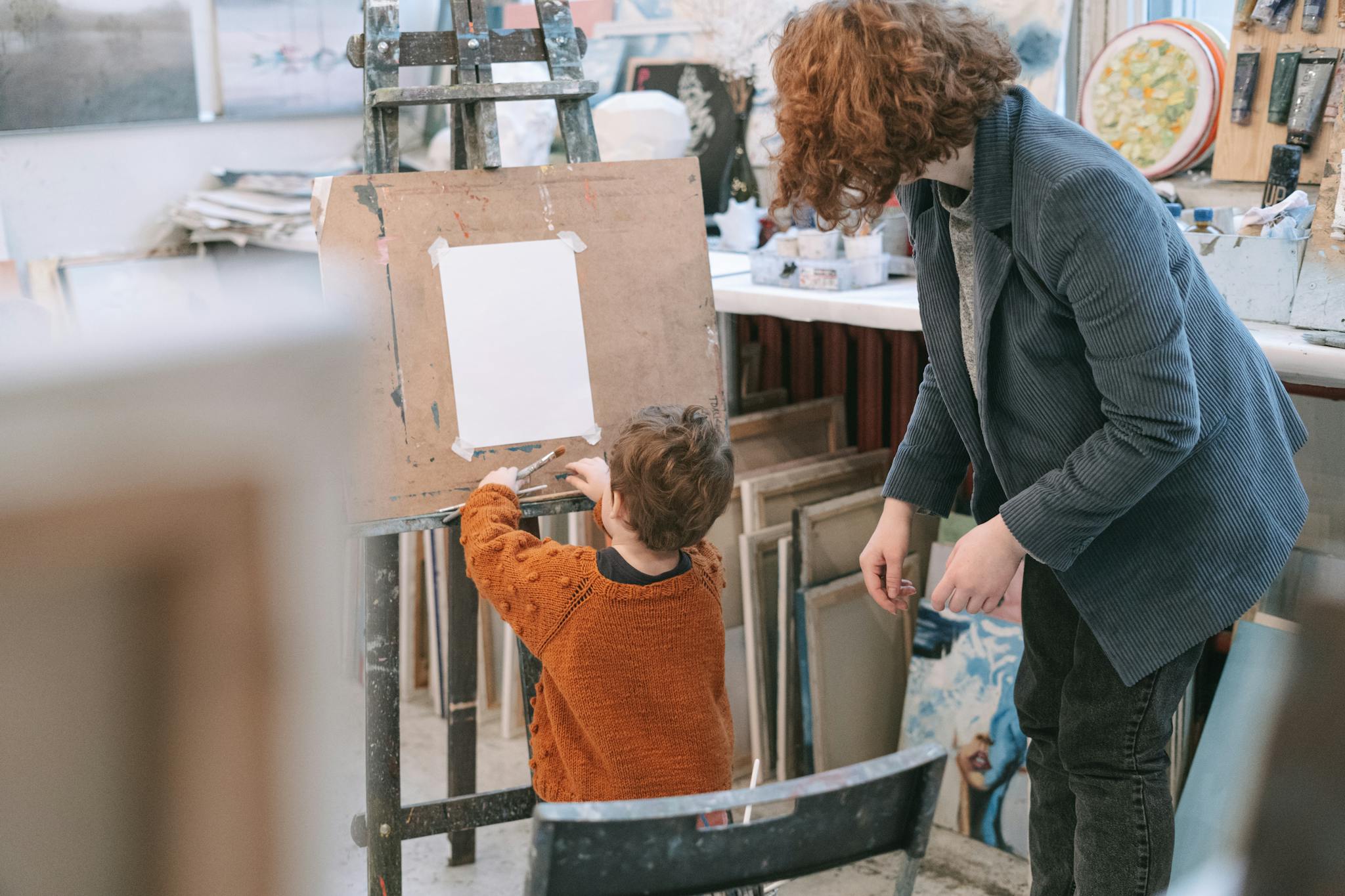 A woman guides a child in painting on an easel, fostering creativity and learning indoors.